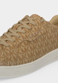 Basket beige Michael Kors à motif monogramme, lacets assortis, semelle blanche et logo métallique de la marque sur le côté.