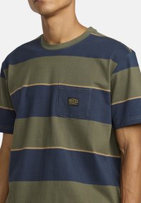 Cotton t-shirt with navy and olive horizontal stripes, featuring a small chest pocket and a logo patch in yellow and black.