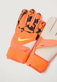 Brankárske rukavice Nike v jasne oranžovej farbe s čiernym geometrickým dizajnom. Obsahujú textúrovaný grip, polstrovanú dlaň a nastaviteľné zápästné popruhy.
