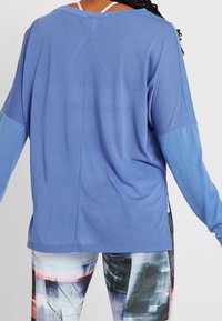 Lös passform, långärmad topp i ljusblått med texturerat tyg. Har en rundad halsringning och kontrasterande ärmfärg.