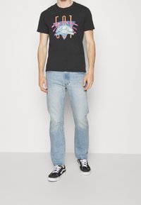 Mustat graafiset t-paidat, joissa on värikäs printti, vaaleansiniset farkut ja mustat tennarit. Rentoa pukeutumista, lyhyet hihat ja pyöreä pääntie.