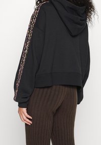 Felpa nera corta con cappuccio spazioso, caratterizzata da strisce a stampa leopardo multicolore lungo le maniche. Realizzata in tessuto morbido.