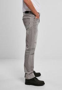 Jeans de mezclilla gris para hombre con corte recto, presentan bolsillos delanteros y traseros y un ligero desgastado. Combinados con botas negras con cordones.
