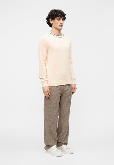 Hele roosa pika varrukaga särk rohelise kraevastriibuga, kombinatsioonis pruunide tekstuursete laiade pükstega ja valgete tennistega.