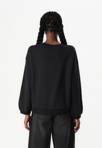 Svart oversized sweatshirt med rund hals, nedfallende skuldre og ribbet avslutning. Har en glatt tekstur og lange ermer.