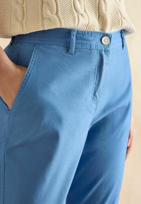 Jasnoniebieskie spodnie z bawełny o gładkiej fakturze. Posiadają boczne kieszenie i zapięcie na guzik w talii.