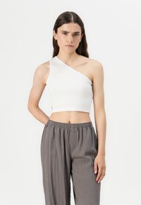 Crop top blanc à côtes avec un design une épaule, caractérisé par une silhouette ajustée et des détails sur les coutures latérales, associé à un pantalon gris ample.