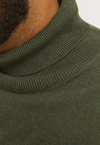 Oliwkowy sweter z golfem wykonany z miękkiego dzianinowego materiału. Posiada prążkowany kołnierz i gładką fakturę z subtelnymi różnicami w kolorze.