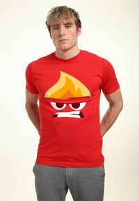 Rød T-shirt med korte ærmer, der har et grafisk design af et tegneserie-flammeansigt med vrede øjne og en sur min. Blødt bomuldsstof.