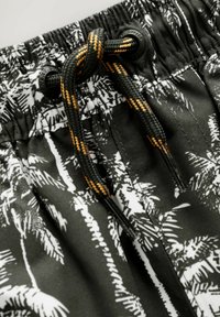 Shorts de bain noirs avec un motif de palmiers blancs, dotés d'une taille élastique noire et d'un cordon de serrage avec une rayure orange.