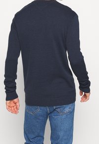 Pull en maille bleu marine pour homme avec des poignets et un ourlet côtelés, un col ras du cou et une finition texturée, associé à un jean en denim.