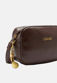 Smeđa kožna torba s teksturiranom završnom obradom, pravokutnog oblika, zlatnim logotipom "LIUJO" i zlatnim hardverom s privjeskom.