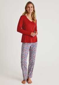 Rode blouse met lange mouwen en een V-hals, gecombineerd met blauwe broeken met een bloemenprint in rood en blauw. Lichtgewicht, casual loungekleding.