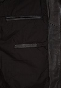 Zwart stoffen jack interieur met twee horizontale leren afgewerkte zakken en een verticale leren paneel aan de rechterkant.