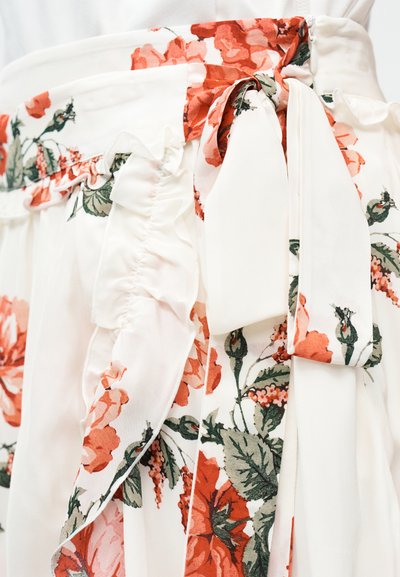 Λευκή υφασμάτινη φούστα με κόκκινο λουλουδάτο σχέδιο και δεμένο φιόγκο στη μέση, με βολάν στις άκρες.