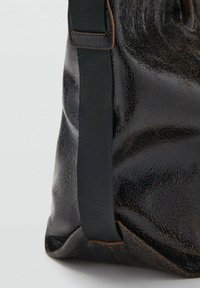 Borsa in pelle nera con texture, finitura lucida, dotata di una tracolla in tessuto scuro e dettagli in cucitura marrone. Vista laterale che mostra la forma e il materiale.