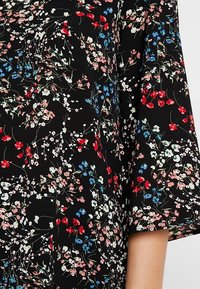 Svart tyg med färgglada blommönster i röd, rosa, vit och blå, med en lös passform på ärmarna.