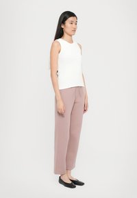 White sleeveless top paired with blush pink wide-leg pants and black slip-on shoes. Smooth texture, simple design, and straight silhouette.