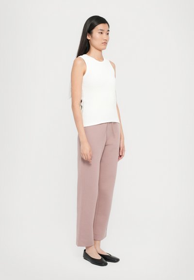 Hvit ermeløs topp parret med blush rosa vide bukser og svarte slip-on sko. Glatt tekstur, enkelt design og rett silhuett.