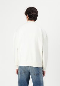 Sweatshirt en coton blanc avec une coupe décontractée, épaules tombantes et ourlet côtelé, associé à un jean en denim bleu clair.