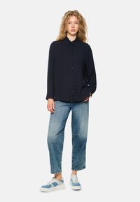 Navy button-up blouse with long sleeves, paired with light blue relaxed-fit jeans and blue-accented sneakers.