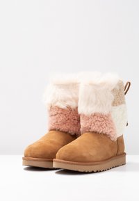 Beżowe botki za kostkę z zamszu z teksturowaną futrzaną cholewką, zawierające kremowe, różowe i beżowe panele, miękki mankiet oraz gumową podeszwę.