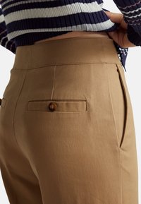 Lichtbruine op maat gemaakte broek met een zachte textuur, voorzien van zijzakken en een knoopdetail op de achterzak. Middenhoge taille.