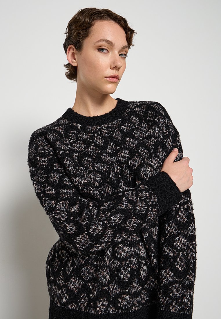 Zwarte gebreide trui met een textuurpatroon in grijstinten en crème. Ronde halslijn en lange, smalle mouwen.