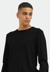 Maglione nero a maniche lunghe lavorato a maglia con collo rotondo. Il tessuto sembra morbido, con una trama liscia e dettagli di cucitura delicati lungo le cuciture.