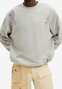 Sudadera gris hecha de algodón suave, con acentos ilustrados en las mangas y el dobladillo, con un corte relajado y un clásico cuello redondo.