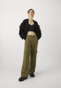 Zwarte gebreide cardigan met franjes, cropped zwart topje, kaki wijde cargobroek en chunky zwarte platform schoenen.