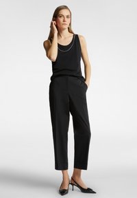 Zwarte tanktop met een ronde halslijn en subtiele kettingdetail, gecombineerd met losse zwarte broeken met omslagonderhems en zijzakken.