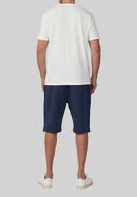 Witte katoenen t-shirt gecombineerd met marineblauwe shorts. De shorts hebben een zijzak, een zachte textuur en een relaxte pasvorm. Witte sneakers maken de look compleet.