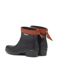 Botas de goma negras hasta el tobillo con un acento de cuero marrón en la parte superior, que presentan un pequeño tacón y un detalle decorativo de lazo en la parte posterior.