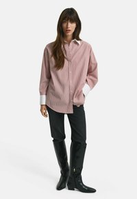 Rot-weiß gestreiftes Shirt mit einem weißen Kragen, kombiniert mit schwarzen, eng anliegenden Hosen und kniehohen schwarzen Stiefeln. Glatter Stoff mit lockerer Passform.