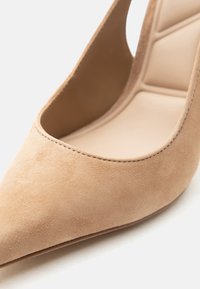 Escarpin à talon haut en daim beige avec bout pointu, doublure intérieure en cuir lisse et coutures nettes le long du bord.