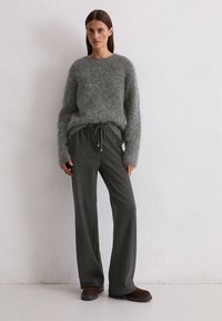 Grijze, fluffy trui met lange mouwen, gecombineerd met donkergrijze, wijde broeken met een verstelbare drawstring tailleband en zilveren accenten.