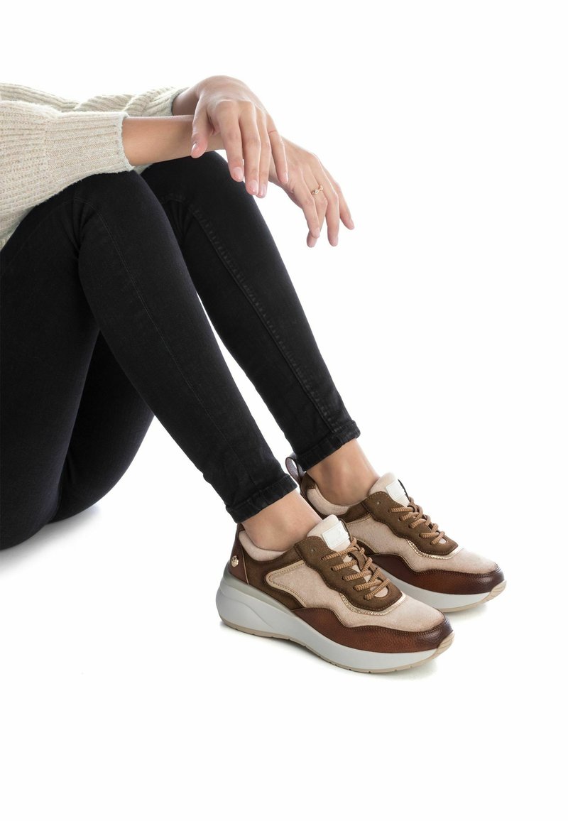 Zapatillas marrones y beige con materiales de ante y cuero, suela gruesa, diseño de cordones y acento en la lengüeta blanca.