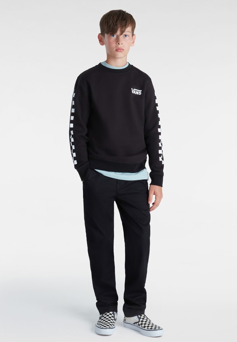 Sudadera negra con el logo blanco de Vans, combinada con una camiseta de cuello redondo azul claro, pantalones negros y zapatillas de cuadros en blanco y negro.