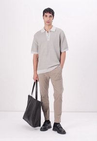 Lys grå kortermet polo med krage, ribbet tekstur. Beige slim-fit bukser og en svart tote bag. Svart sko fullfører looken.