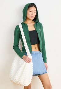 Zelená mikina na zips, čierny crop top, džínsová mini sukňa a biela textúrovaná taška na rameno s hrubým popruhom. Jednoduchý dizajn a ležérny štýl.