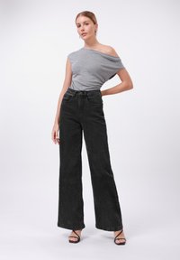 Siva majica s otklonjenim ramenima, crne traperice viskog struka širokih nogavica, glatka denim tekstura, minimalni dodaci, nosi se s crnim sandalama na visoku petu.