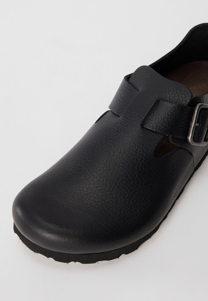 Black leather clog with a smooth texture, curved toe, side cutouts, and an adjustable strap featuring a silver buckle. Rubber sole.