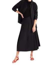 Gonna midi plissettata nera con vita alta, abbinata a una camicia nera ampia e sandali rossi con cinturini e suola bianca.