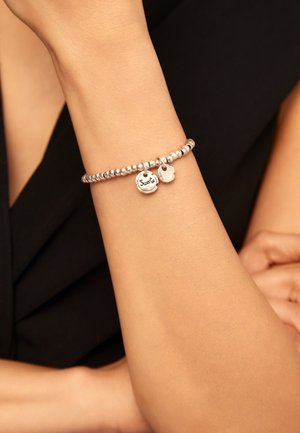 Pulsera de cuentas plateadas con dos dijes colgantes, uno grabado con "Sura". Textura suave con un acabado pulido.