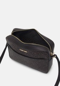 Torebka crossbody Calvin Klein w ciemnobrązowej skórze z wzorem logo, ze złotymi elementami zamka i przestronnym wnętrzem. Posiada regulowany pasek.