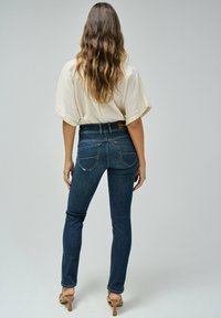 Jeans skinny de color azul oscuro con una cintura alta, que presentan bolsillos traseros con costura curva y una etiqueta de cuero marrón en la cinturilla.