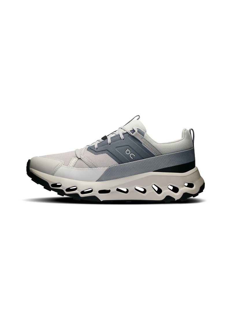 Zapatillas deportivas con una parte superior de malla ligera en gris y blanco, que presentan una suela gruesa y acolchada con aberturas para ventilación.