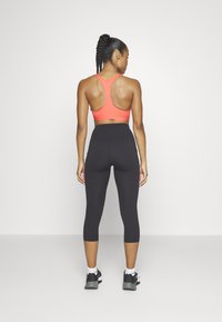 Červená sportovní podprsenka s designem racerback, kombinovaná s černými legínami s vysokým pasem. Hladký povrch a přiléhavý střih usnadňují pohyb.