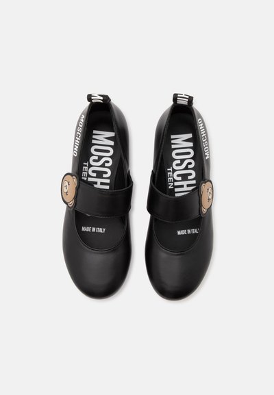 Chaussures Mary Jane noires avec une décoration visage d'ours sur les brides et un marquage blanc MOSCHINO à l'intérieur et sur les languettes de talon.